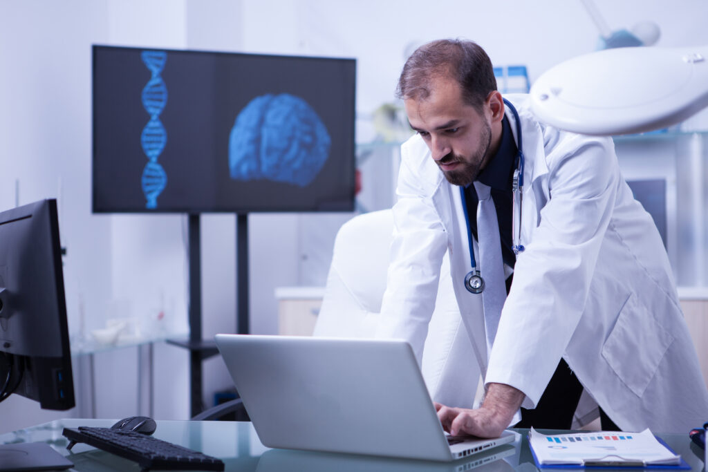 doctor working on laptop with brain image in the background